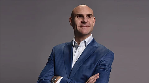 Jeff Dodds, CEO der Formel E, steht mit verschränkten Armen und lächelnd vor einem neutralen grauen Hintergrund, gekleidet in einem blauen Sakko und weißem Hemd.