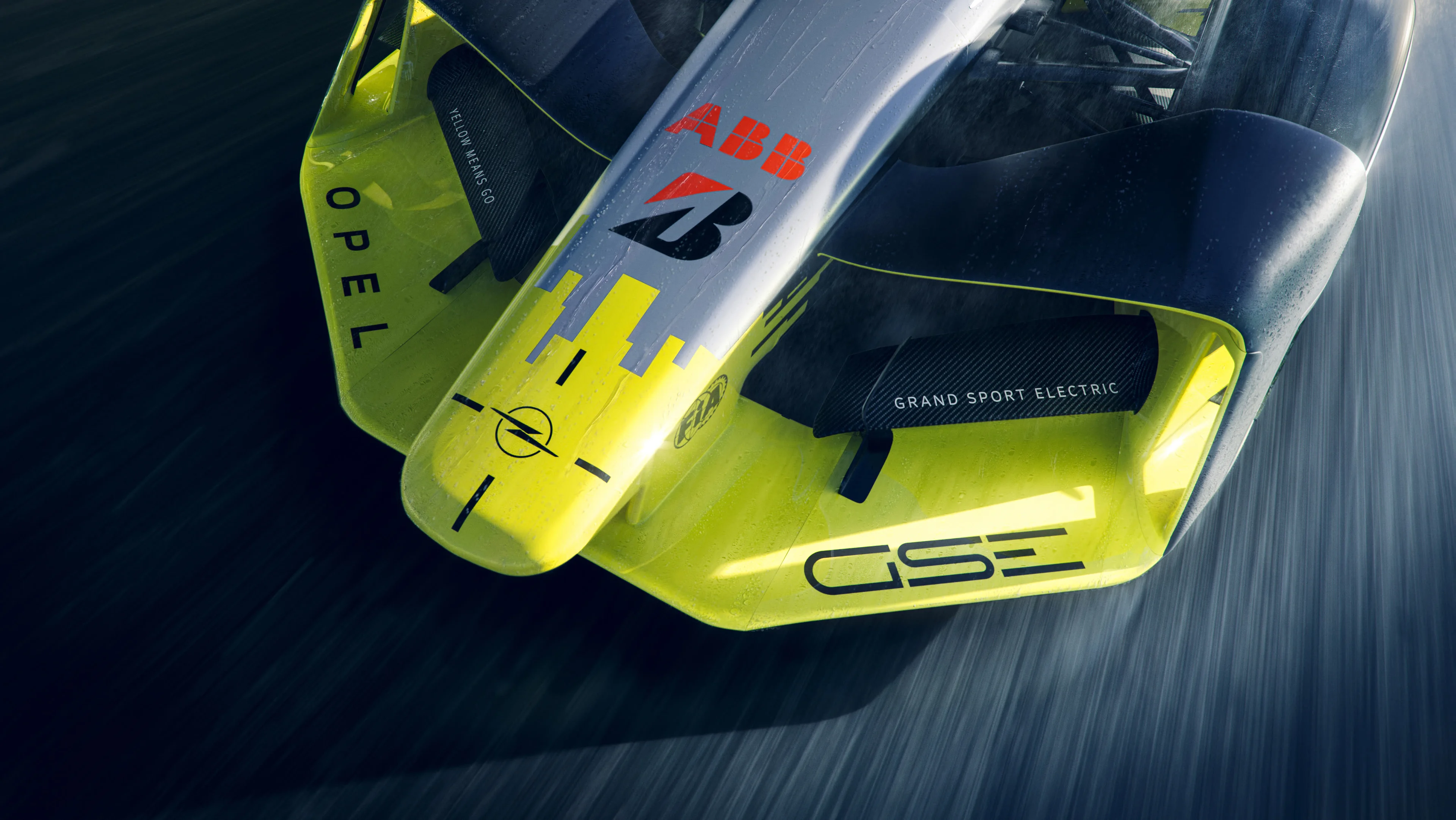 Close-up of the wet yellow and silver nose and front wing of the Opel GSE Formula E car at speed, showing "OPEL", "GSE" and the Opel Blitz logo.