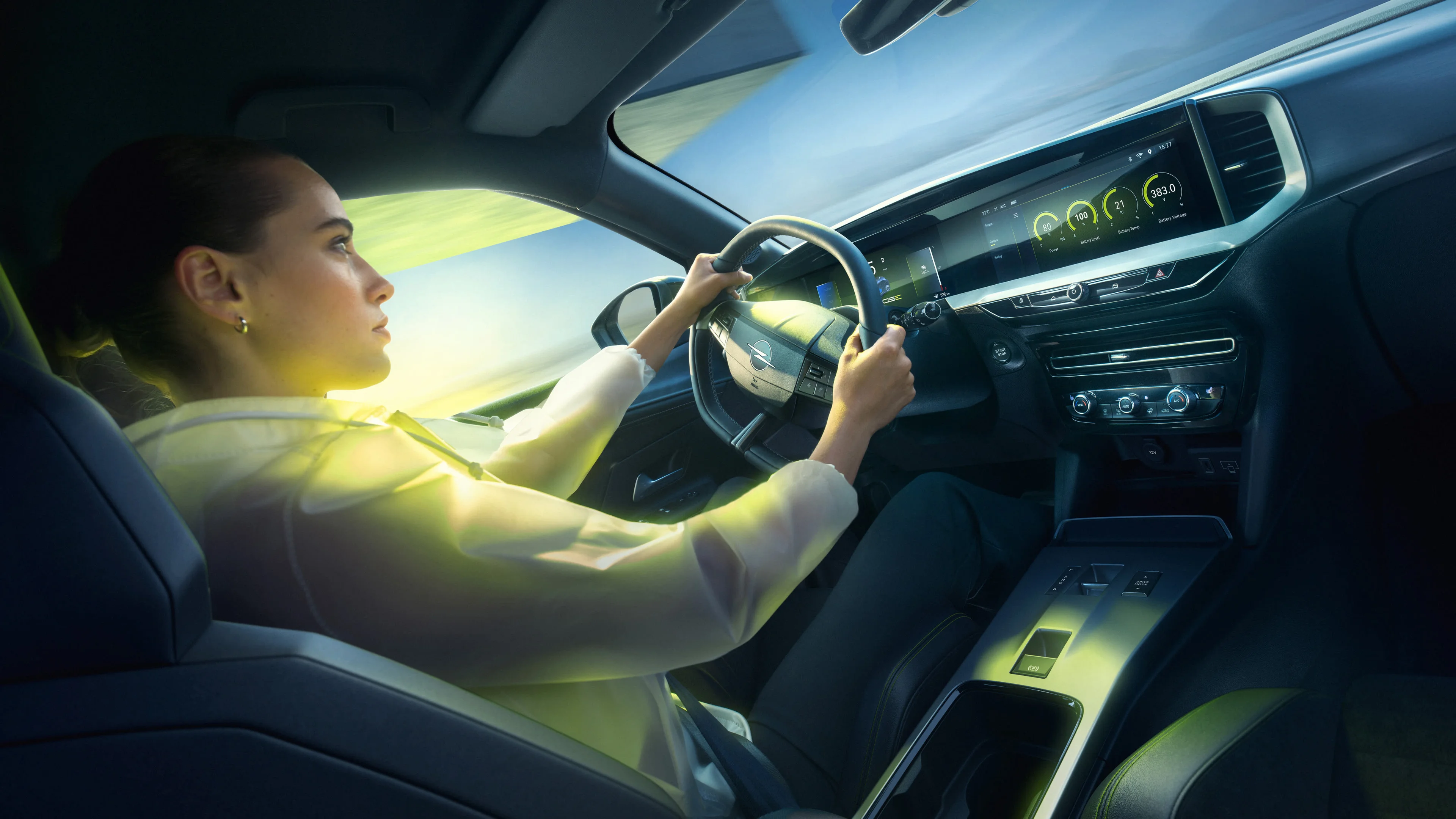 A woman driving an Opel Mokka GSE, seen from the passenger side, with both hands on the steering wheel and the car's two digital displays lit up on the dashboard beside her.