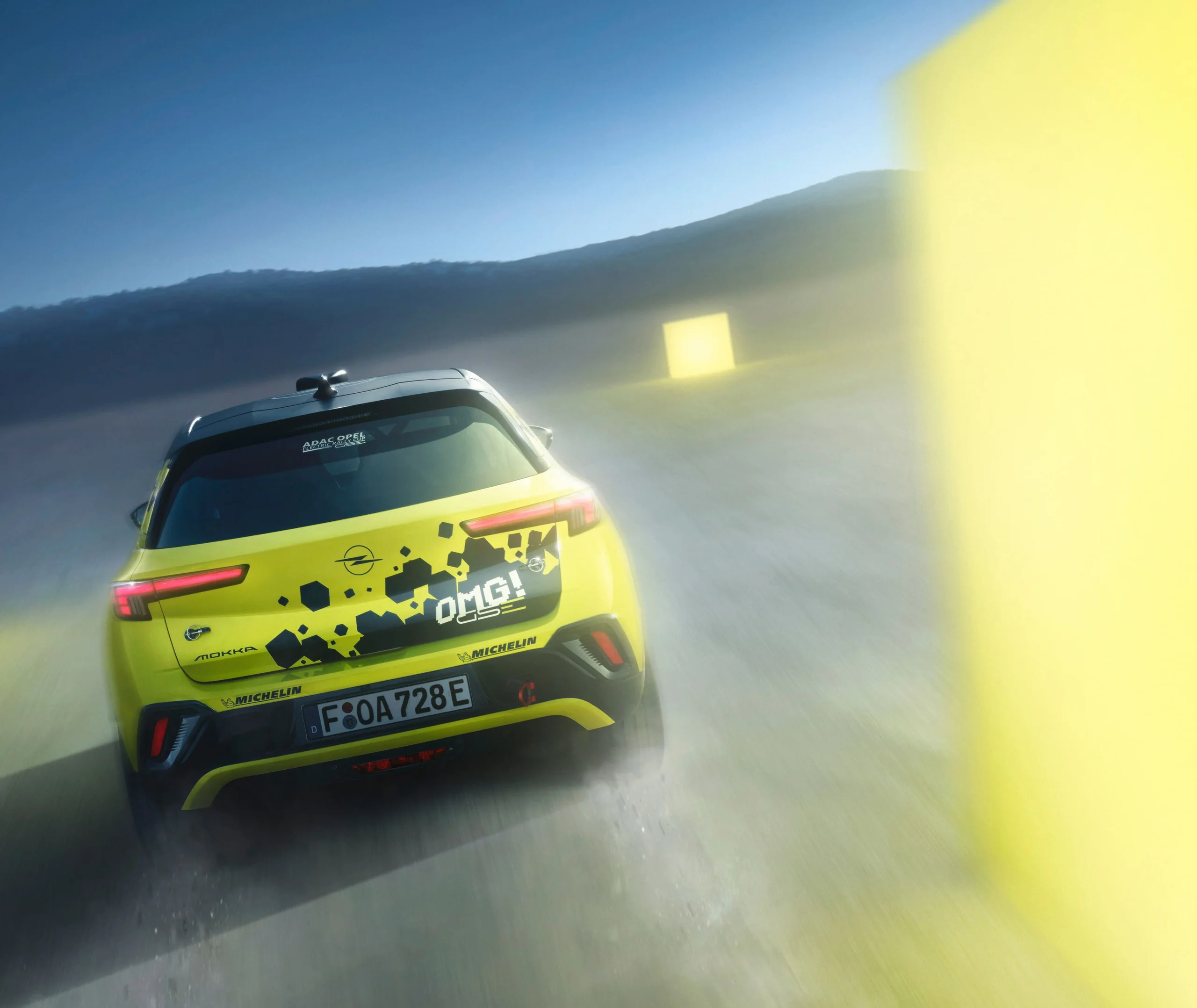Neon yellow Opel Mokka GSE Rally car seen straight from behind driving away at dusk, tail lights lit, with yellow course markers blurred past on either side and a dark ridge on the horizon.